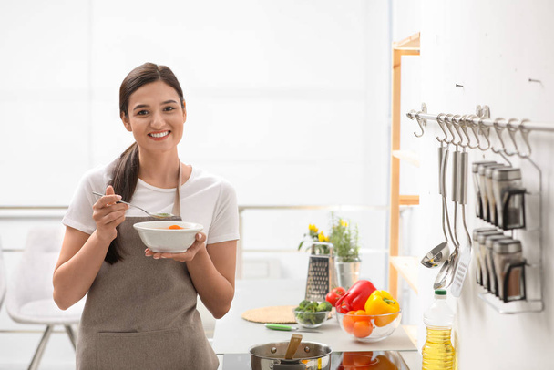 Young woman eating tasty vegetable soup in kitchen - Photo, image