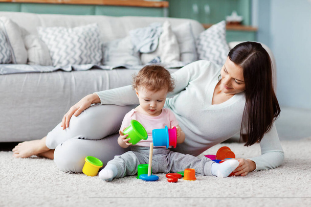 Little girl and mom play on the floor on a light carpet with bright toys, build a tower - Photo, Image