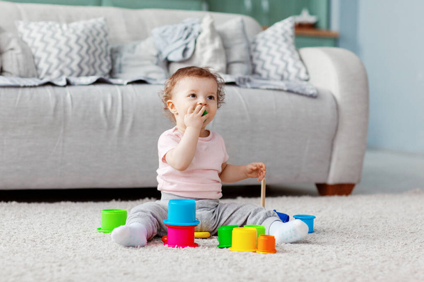 das Kind spielt auf dem Boden auf einem hellen Teppich mit hellem Spielzeug, baut einen Turm - Foto, Bild