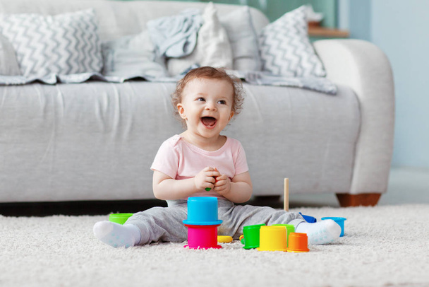 Ребенок играет на полу на светлом ковре с яркими игрушками, строит башню
 - Фото, изображение