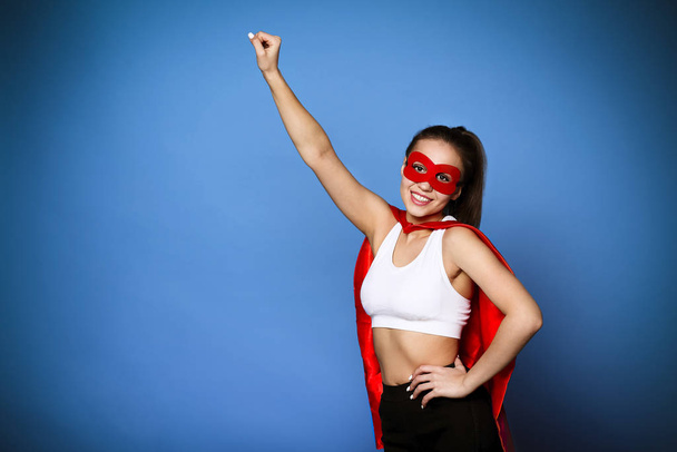 Весела жінка в супергеройському плащі тримає підняту руку
 - Фото, зображення