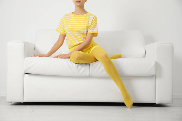 Woman wearing yellow tights sitting on sofa indoors, closeup - 写真・画像