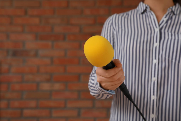 Journalist with microphone near brick wall, closeup. Space for text - Φωτογραφία, εικόνα