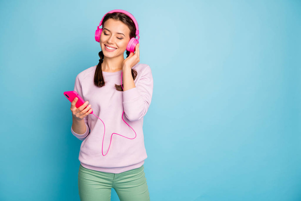 Photo of pretty lady holding telephone cool bright earphones on ears listening youth radio eyes closed wear casual stylish pink pullover trousers isolated blue color background - Foto, afbeelding