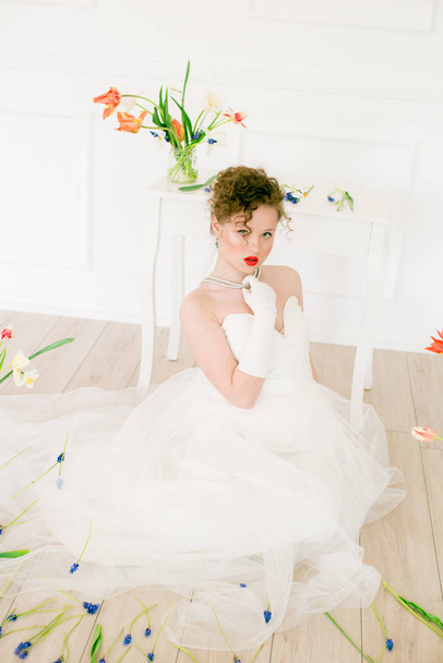 Ελκυστική νεαρή νύφη με λευκό φόρεμα σε ένα φωτεινό στούντιο άνοιξη διακοσμημένο με τουλίπες. Ομορφιά και μόδα - Φωτογραφία, εικόνα