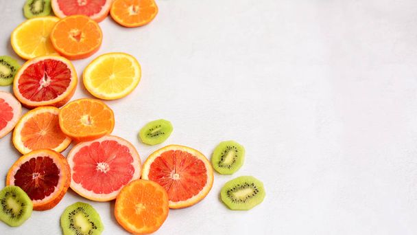 Close-up of sliced red orange, tangerines, green kiwi and grapefruit on a light gray background. Side space for lettering and design. - Photo, Image