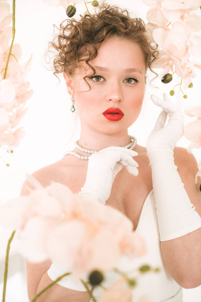 Attractive young bride in a white dress in a light spring studio with white orchids. Beauty and Fashion - Valokuva, kuva