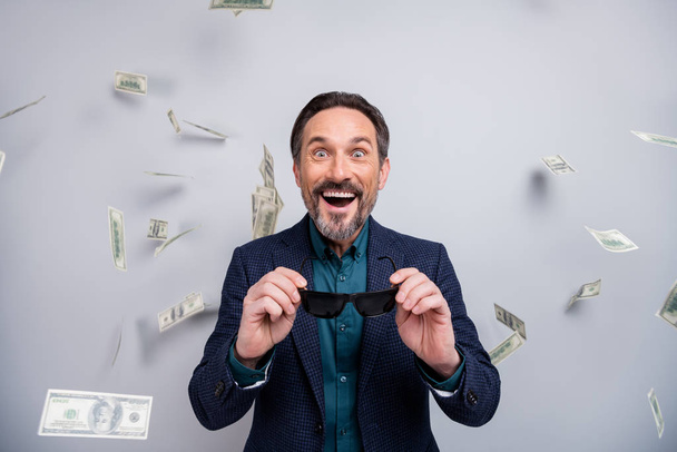 Photo of crazy business mature man speechless watch usa american dollars banknotes falling flying formalwear blazer shirt blue suit sun specs isolated grey color background - Photo, Image