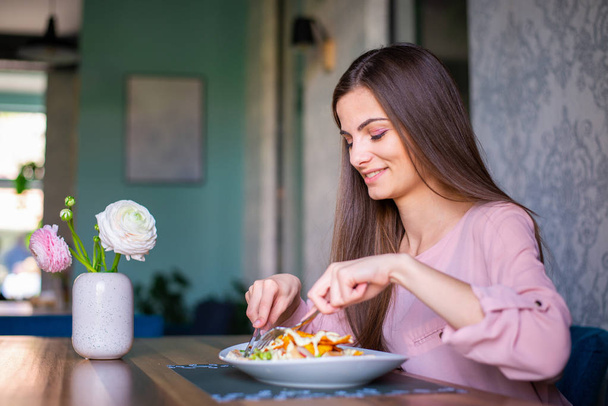 Красивая молодая женщина ест салат в хорошем ресторане
. - Фото, изображение