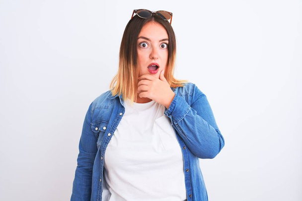 Beautiful woman wearing denim shirt standing over isolated white background Looking fascinated with disbelief, surprise and amazed expression with hands on chin - Foto, Imagem
