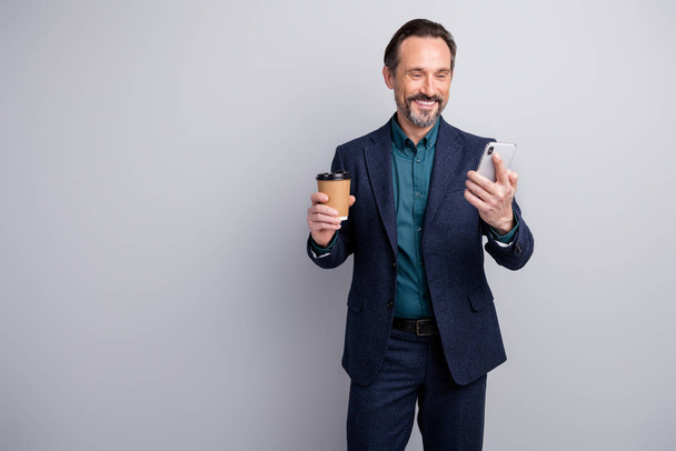 Photo of handsome friendly business man chief hold telephone hands read corporate email drink hot coffee to go formalwear blazer shirt trousers blue suit isolated grey color background - Φωτογραφία, εικόνα