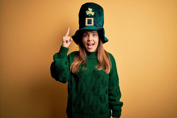 Joven hermosa morena con sombrero verde en la celebración del día de San Patricio señalando con el dedo hacia arriba con una idea exitosa. Salido y feliz. Número uno.
. - Foto, Imagen
