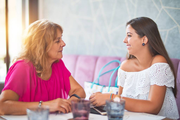 Kaunis äiti ja tytär istuvat ravintolassa puhumassa ja hymyilemässä
 - Valokuva, kuva