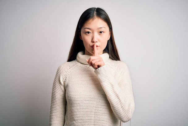 Young beautiful asian woman wearing casual sweater standing over isolated background asking to be quiet with finger on lips. Silence and secret concept. - Foto, Imagen