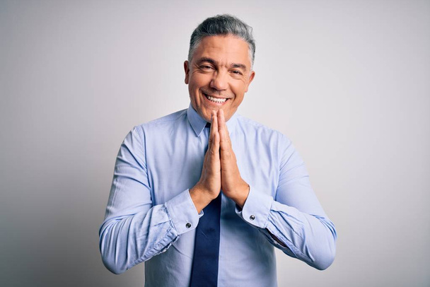Middle age handsome grey-haired business man wearing elegant shirt and tie praying with hands together asking for forgiveness smiling confident. - Photo, image