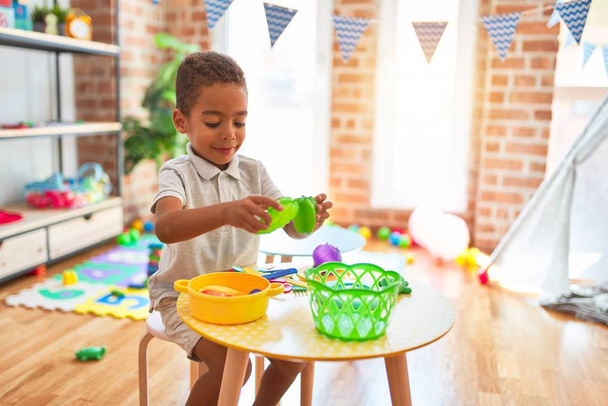 Hermoso niño afroamericano jugando con comida plástica y juguete de cubiertos en el jardín de infantes
 - Foto, Imagen