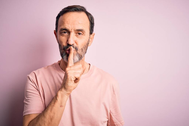Hombre alzado de mediana edad que usa una camiseta casual de pie sobre un fondo rosa aislado que pide estar tranquilo con el dedo en los labios. Silencio y concepto secreto
. - Foto, imagen