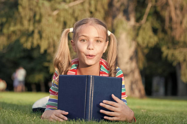 Adorable bookworm. School time. Developing caring learners who are actively growing and achieving. Little child reading book. Schoolgirl reading stories relaxing green lawn. Cute pupil enjoy reading - Photo, Image