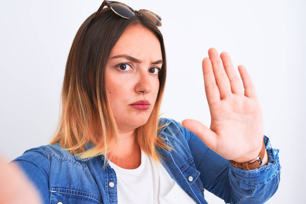 Молодая красивая женщина в джинсовой рубашке стоя на изолированном белом фоне с открытой рукой делать знак стоп с серьезным и уверенным выражением лица, защитный жест
 - Фото, изображение