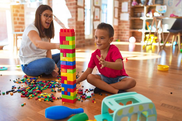 Jonge mooie leraar en peuter spelen met bouwstenen rond veel speelgoed op de kleuterschool - Foto, afbeelding