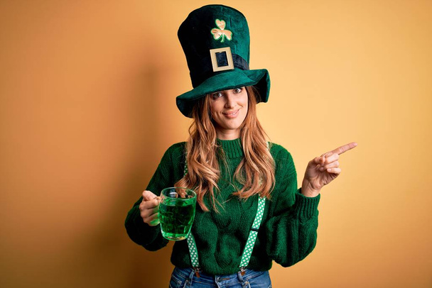 Kaunis nainen yllään hattu juomapurkki vihreää juomaa juhlii pyhimys patricks päivä erittäin onnellinen osoittaa käsin ja sormella sivulle
 - Valokuva, kuva