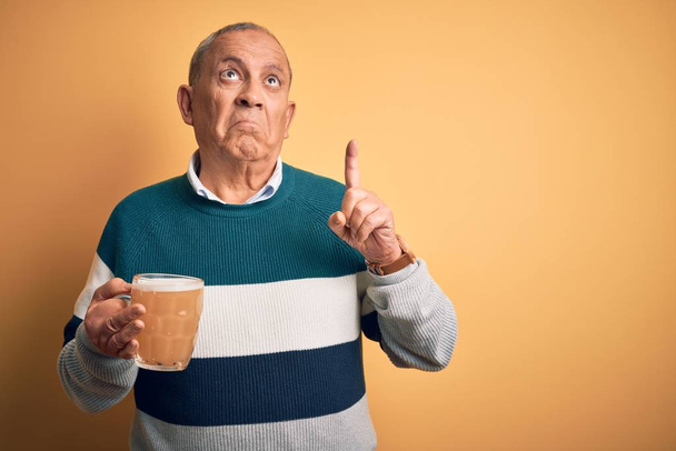 Senior jóképű férfi iszik üveg sör felett áll elszigetelt sárga háttér felmutat néz szomorú és ideges, jelezve irányt ujjak, boldogtalan és depressziós. - Fotó, kép