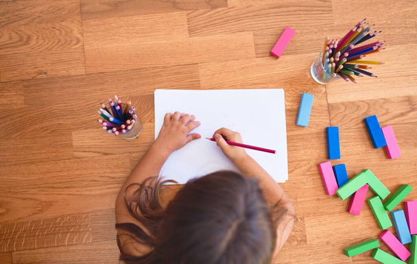 Adorable toddler lying down on the floor drawing using paper and pencils at kindergarten - Foto, Imagen
