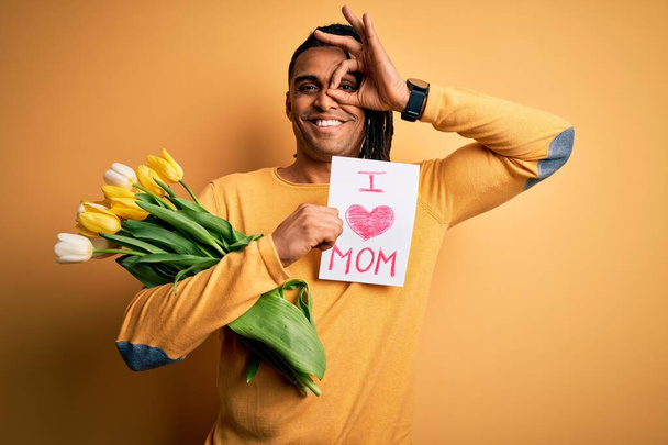 Afrikai amerikai férfi gazdaság szerelem anya üzenet papír és tulipán ünneplő anyák napja boldog arccal mosolygó csinál rendben jel kézzel a szemen keresztül néz az ujjakon - Fotó, kép