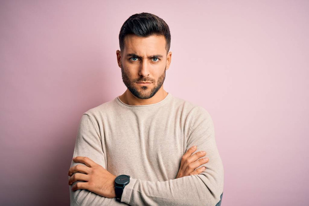 Young handsome man wearing casual sweater standing over isolated pink background skeptic and nervous, disapproving expression on face with crossed arms. Negative person. - 写真・画像