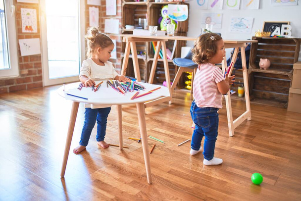 Urocze maluchy bawiące się dużą ilością kolorowych ołówków na stole w przedszkolu - Zdjęcie, obraz