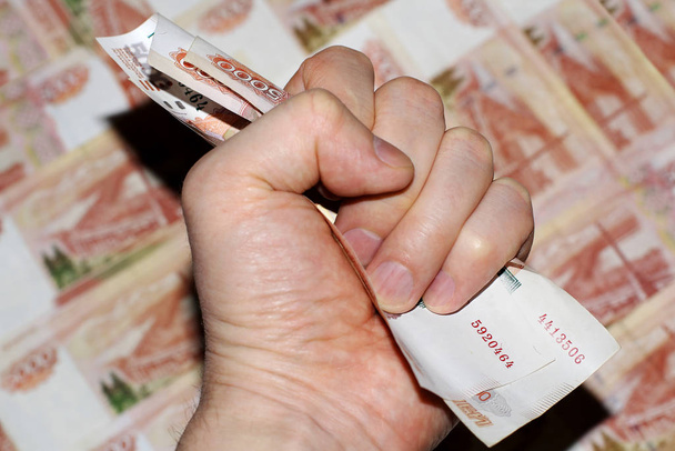 La mano agarra el dinero en su puño. Billetes en cinco mil rublos rusos, colores rojo y blanco. La vista desde arriba
. - Foto, imagen