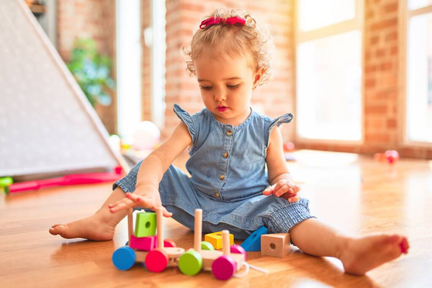 Beautiful caucasian infant playing with toys at colorful playroom. Happy and playful with wooden train pieces at kindergarten. - Photo, Image