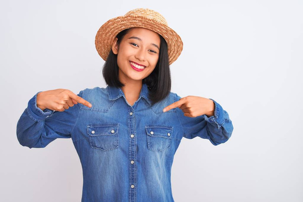Fiatal gyönyörű kínai nő visel farmer ing és kalap felett elszigetelt fehér háttér néz magabiztos mosollyal az arcon, rámutatva önmagára ujjaival büszke és boldog. - Fotó, kép
