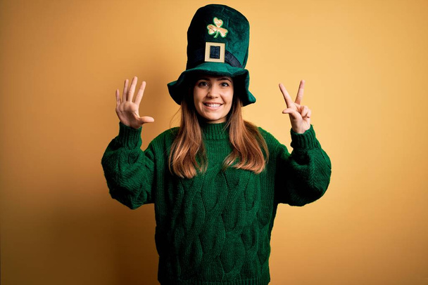 Jovem bela mulher morena usando chapéu verde em st patricks celebração do dia mostrando e apontando para cima com os dedos número oito enquanto sorri confiante e feliz
. - Foto, Imagem