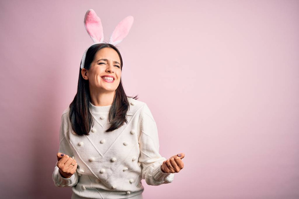 Young caucasian woman wearing cute easter rabbit ears over pink isolated background very happy and excited doing winner gesture with arms raised, smiling and screaming for success. Celebration concept. - Photo, Image