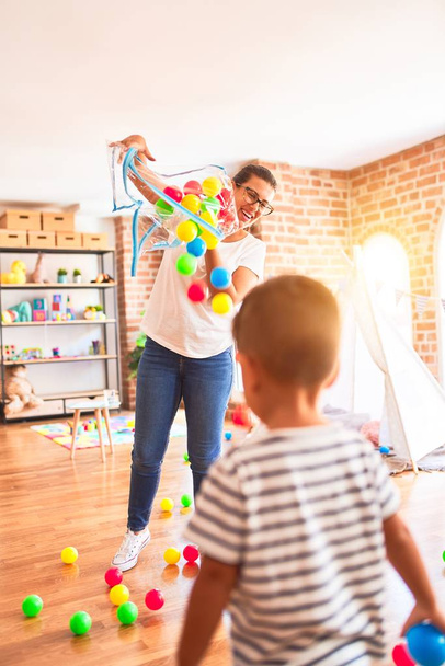 Красивий вчитель і маленький хлопчик грає з кольоровими маленькими кульками в дитячому саду
 - Фото, зображення