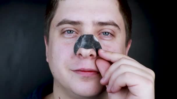 A man puts on and removes a strip for the nose from black dots. Coal cleaning strips from blackheads and comedones. The concept of personal care. - Footage, Video