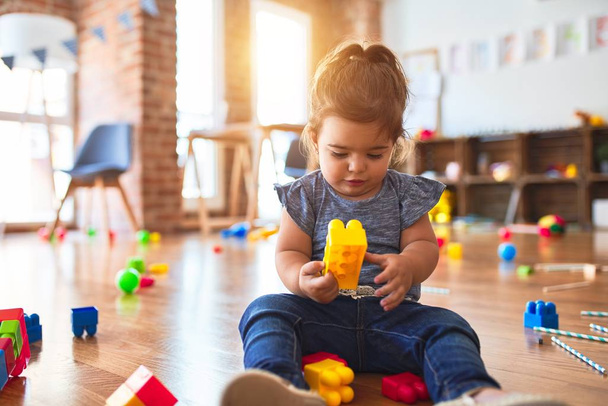 Prachtige peuter zit op de vloer te spelen met bouwstenen speelgoed op de kleuterschool - Foto, afbeelding