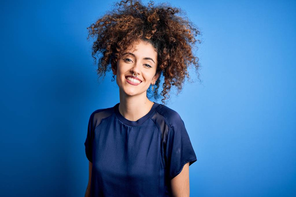 Young beautiful woman with curly hair and piercing wearing casual blue t-shirt with a happy and cool smile on face. Lucky person. - Photo, Image