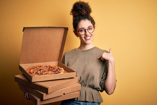 Nuori kaunis nainen kihara tukka ja lävistyksiä tilalla toimitus laatikot Italian pizza yllätys kasvot sormella itselleen
 - Valokuva, kuva