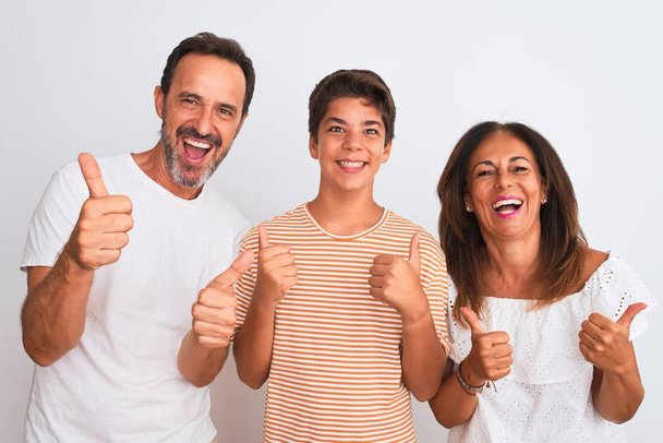 Family of three, mother, father and son standing over white isolated background success sign doing positive gesture with hand, thumbs up smiling and happy. Cheerful expression and winner gesture. - Photo, Image