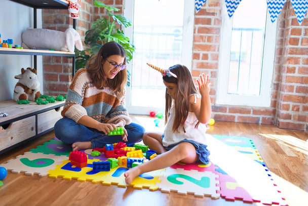 Bella insegnante e bambino che gioca con i blocchi di costruzione giocattolo intorno a un sacco di giocattoli all'asilo
 - Foto, immagini