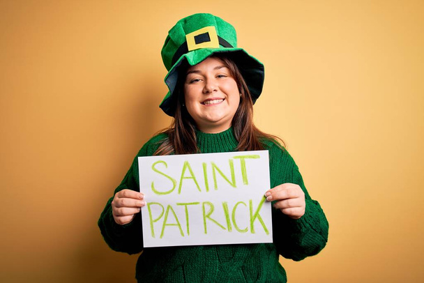 Плюс женщина в зеленой шляпе, празднующая день святого Патрика, держащая плакат со счастливым лицом, стоя и улыбаясь с уверенной улыбкой, показывая зубы
 - Фото, изображение