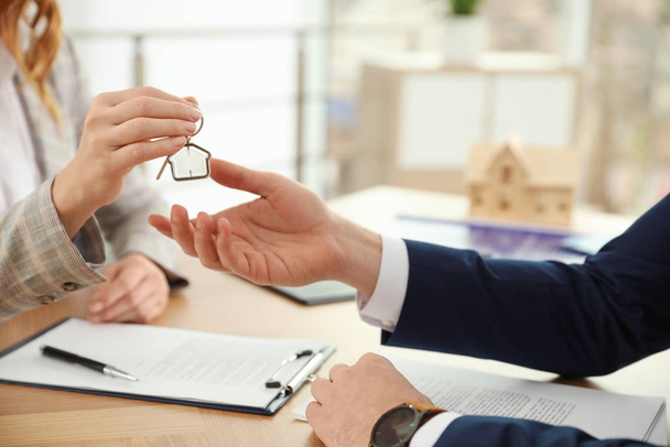 Real estate agent giving key with trinket to client in office, c - Foto, Imagem