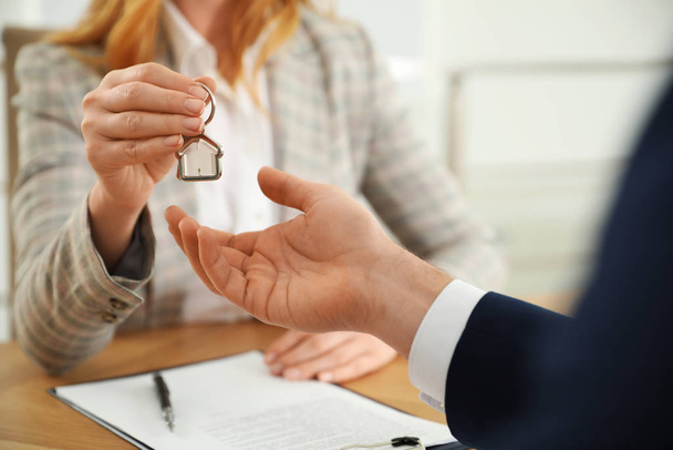 Real estate agent giving key with trinket to client in office, c - Φωτογραφία, εικόνα