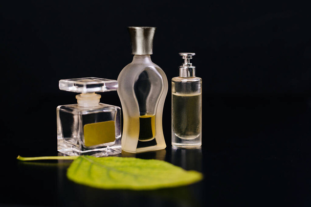 Tres botellas de vidrio con perfume sobre fondo negro. Hoja verde. Aromas de frescura
 - Foto, imagen