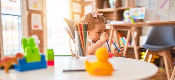 カラフルなプレイルームでおもちゃで遊ぶ美しい白人の幼児。幼稚園の色鉛筆で幸せと遊び心のある図面. - 写真・画像