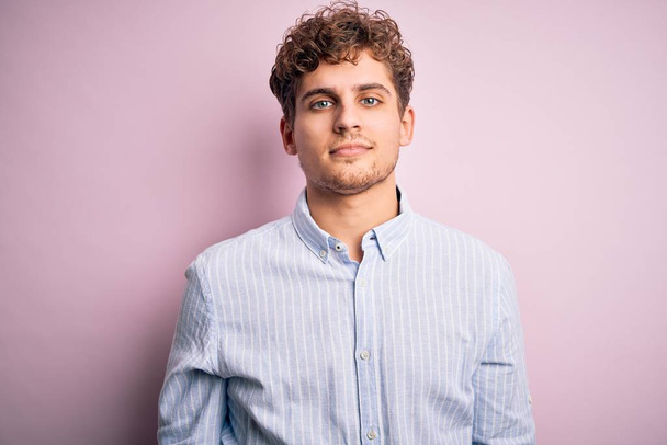 Young blond handsome man with curly hair wearing striped shirt over white background looking sleepy and tired, exhausted for fatigue and hangover, lazy eyes in the morning. - Photo, Image
