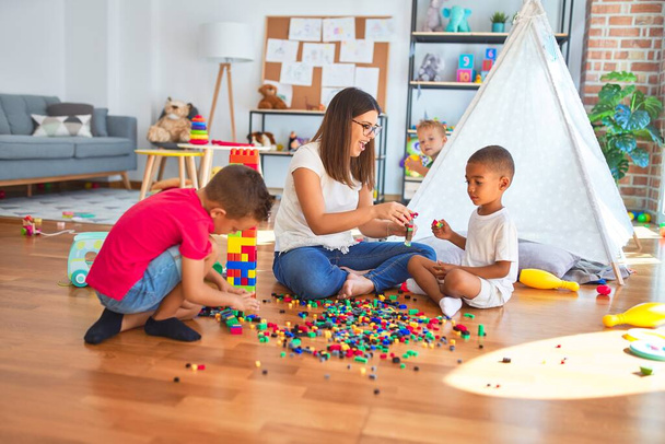 Jeune belle enseignante et tout-petits jouant avec des blocs de construction autour de beaucoup de jouets à la maternelle
 - Photo, image