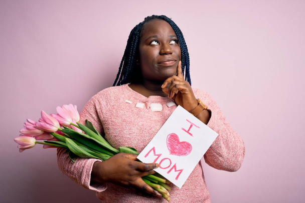 Ayrıca Afrikalı Afrikalı Amerikalı bir kadın anneler gününde sevgi dolu bir mesaj ve laleler taşıyor. Ciddi bir yüz ifadesi var. Soru sormayı düşünüyor. - Fotoğraf, Görsel